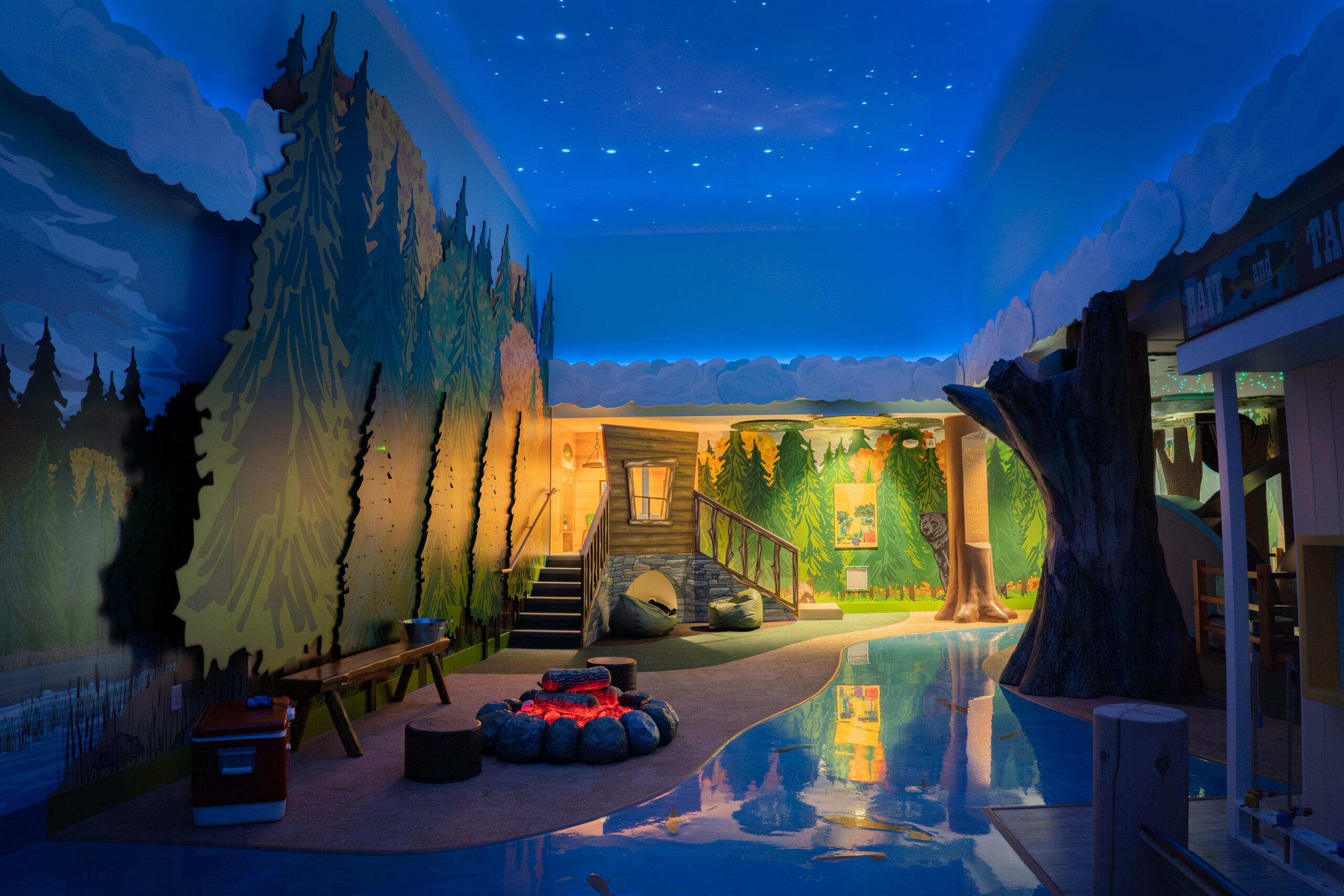 Split Rock Studios Exhibit at Great River Children's Museum. A children's exhibit scene with a cabin, trees, and campfire under a night sky.