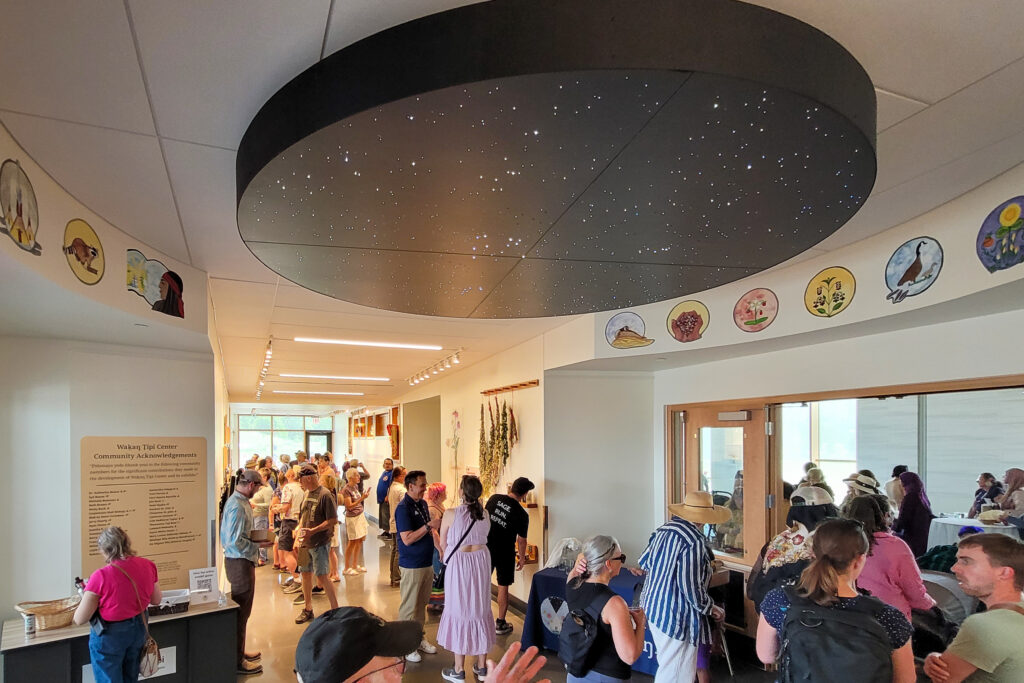 A large crowd inside a building under a black circle art installation