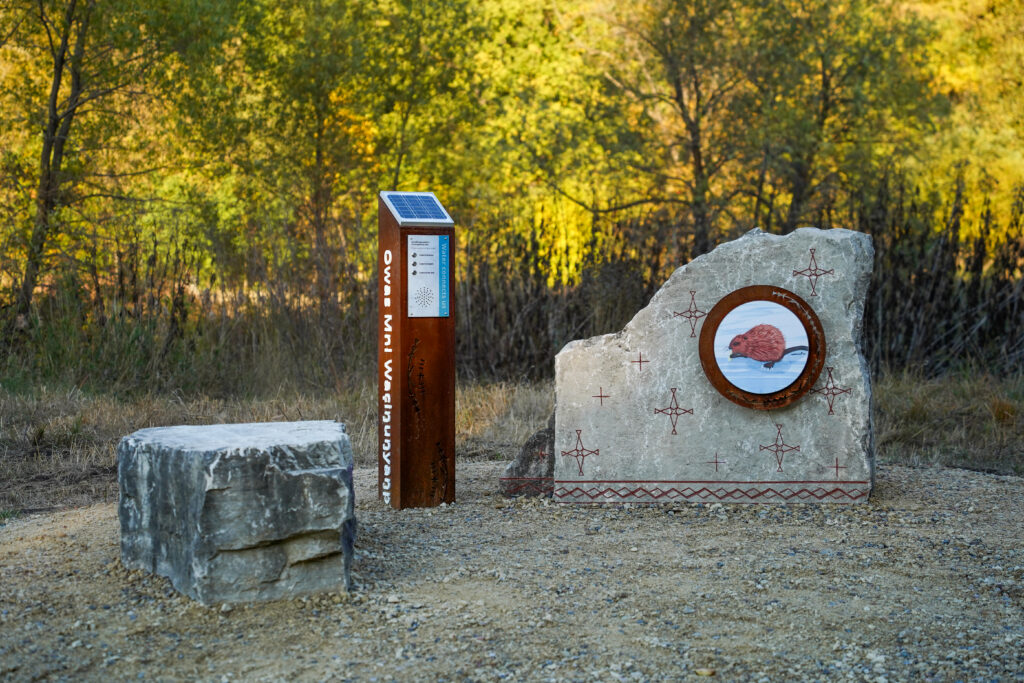 Two boulders next to a metal post outside with trees in the background.